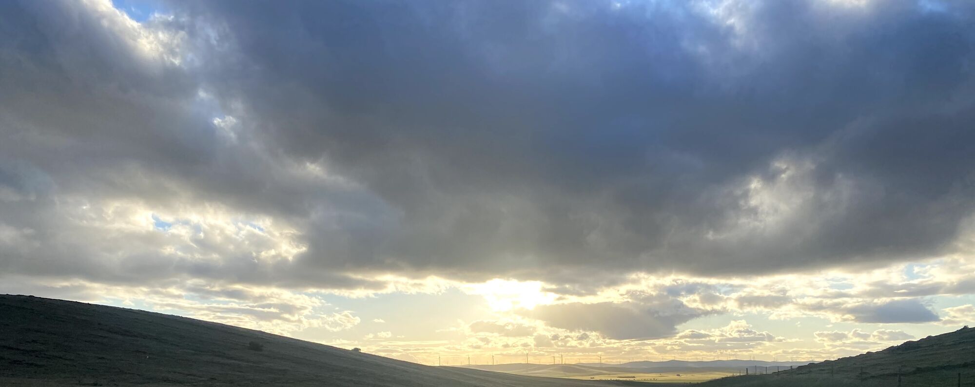 Late sun breaking through cloud over rolling hills and wind turbines